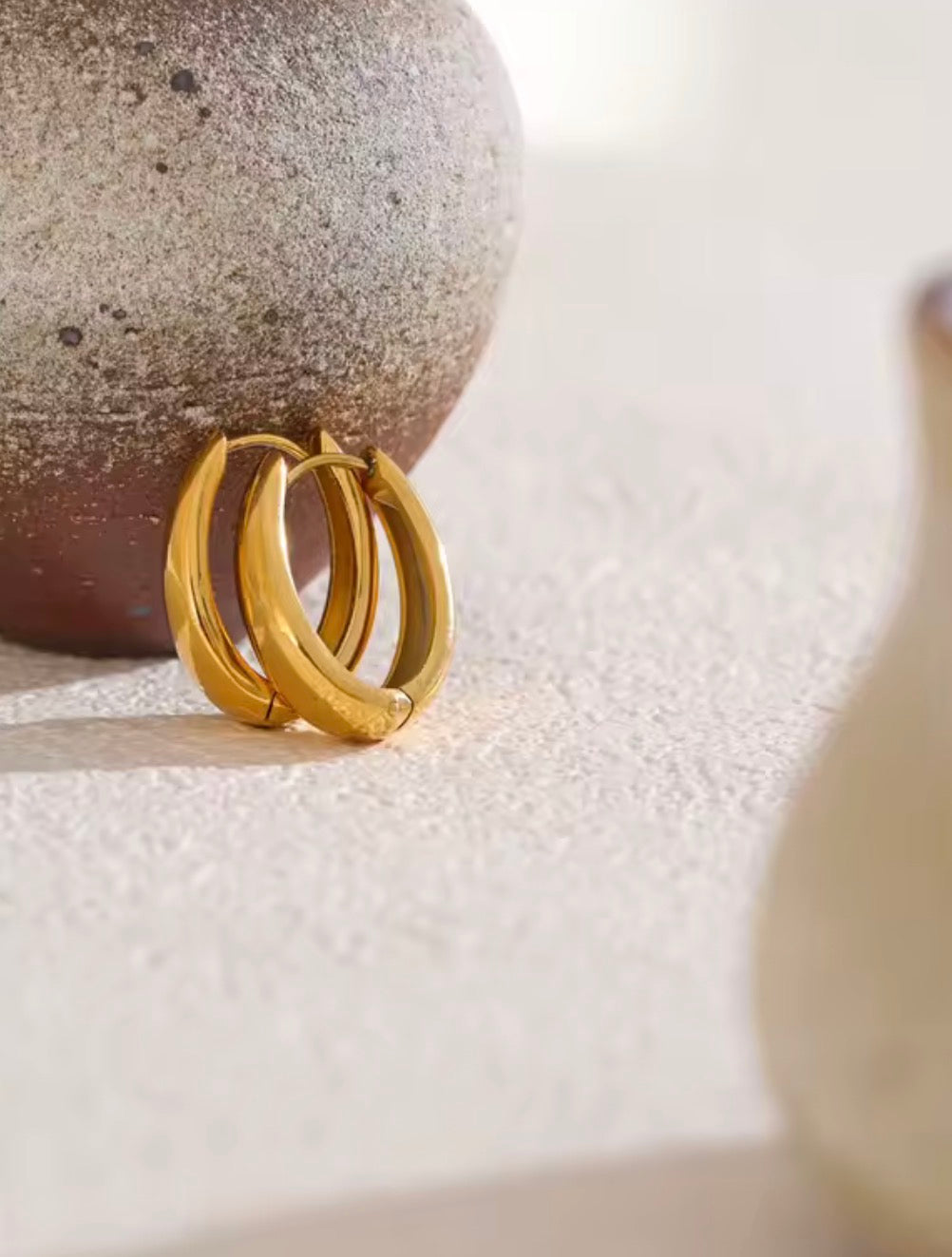 Gold hoop earrings on a textured surface with a stone-like background