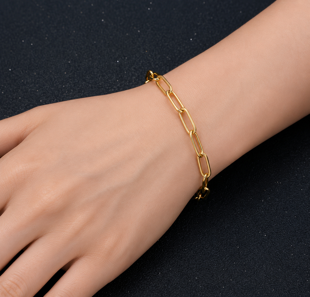 A gold paperclip chain bracelet worn on a person's wrist, shown against a dark textured background.