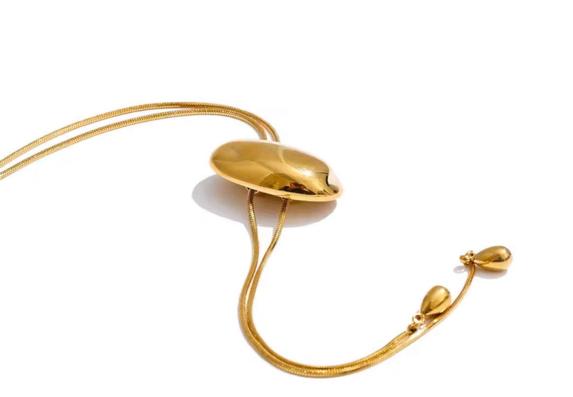 A gold-toned adjustable necklace featuring a smooth, polished oval pendant suspended from a delicate snake chain, shown on a plain white background.