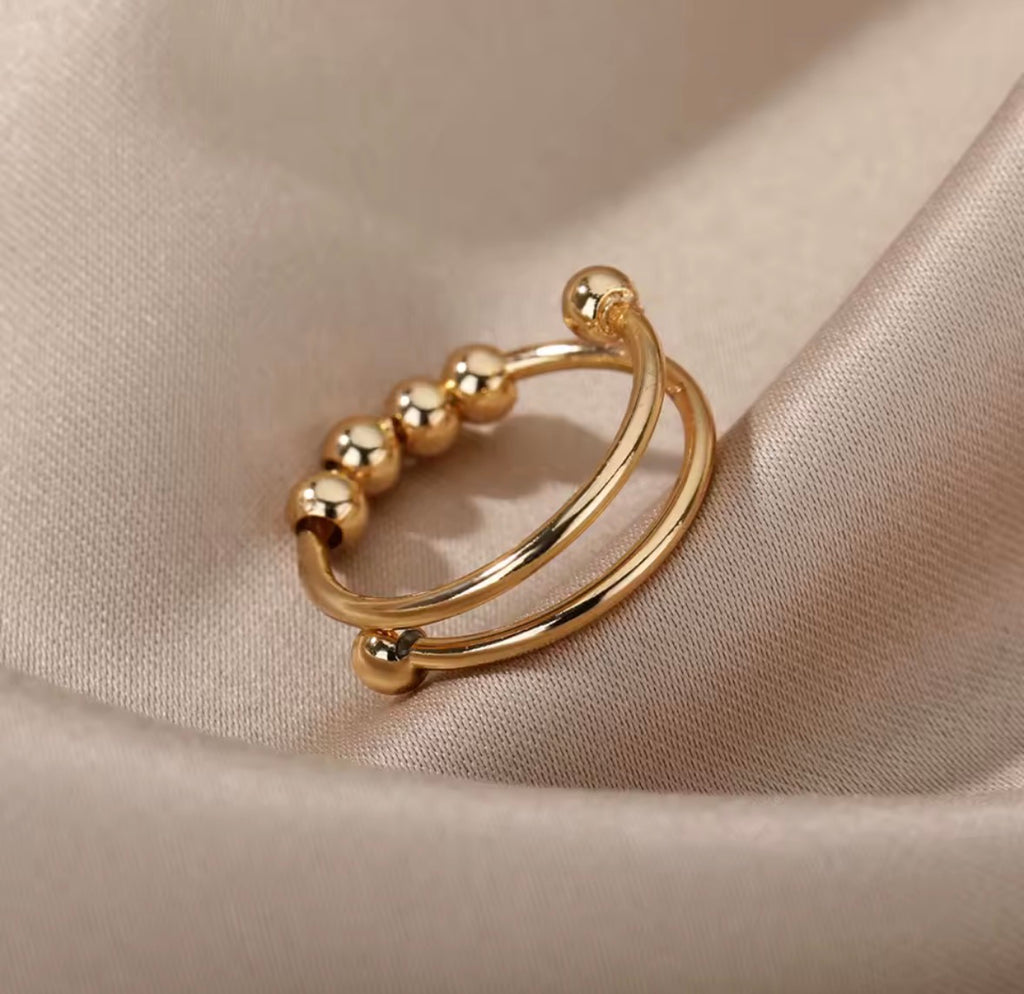 Anti-Anxiety Spinner Ring Gold hoop earring with small beads on a beige fabric background