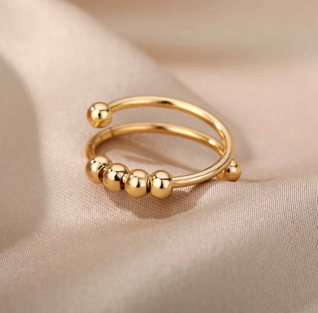 Anti-Anxiety Spinner Ring Gold ring with bead details on a beige fabric background
