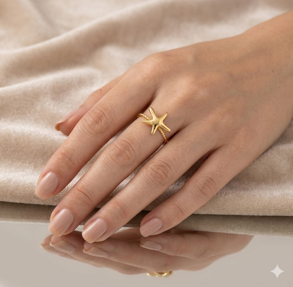 The Amalina Ring Hand wearing a gold star-shaped ring on a beige fabric background