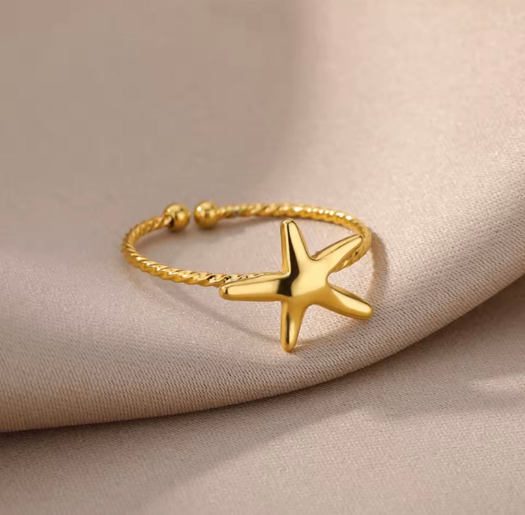 The Amalina Ring   Gold starfish ring on a beige fabric background
