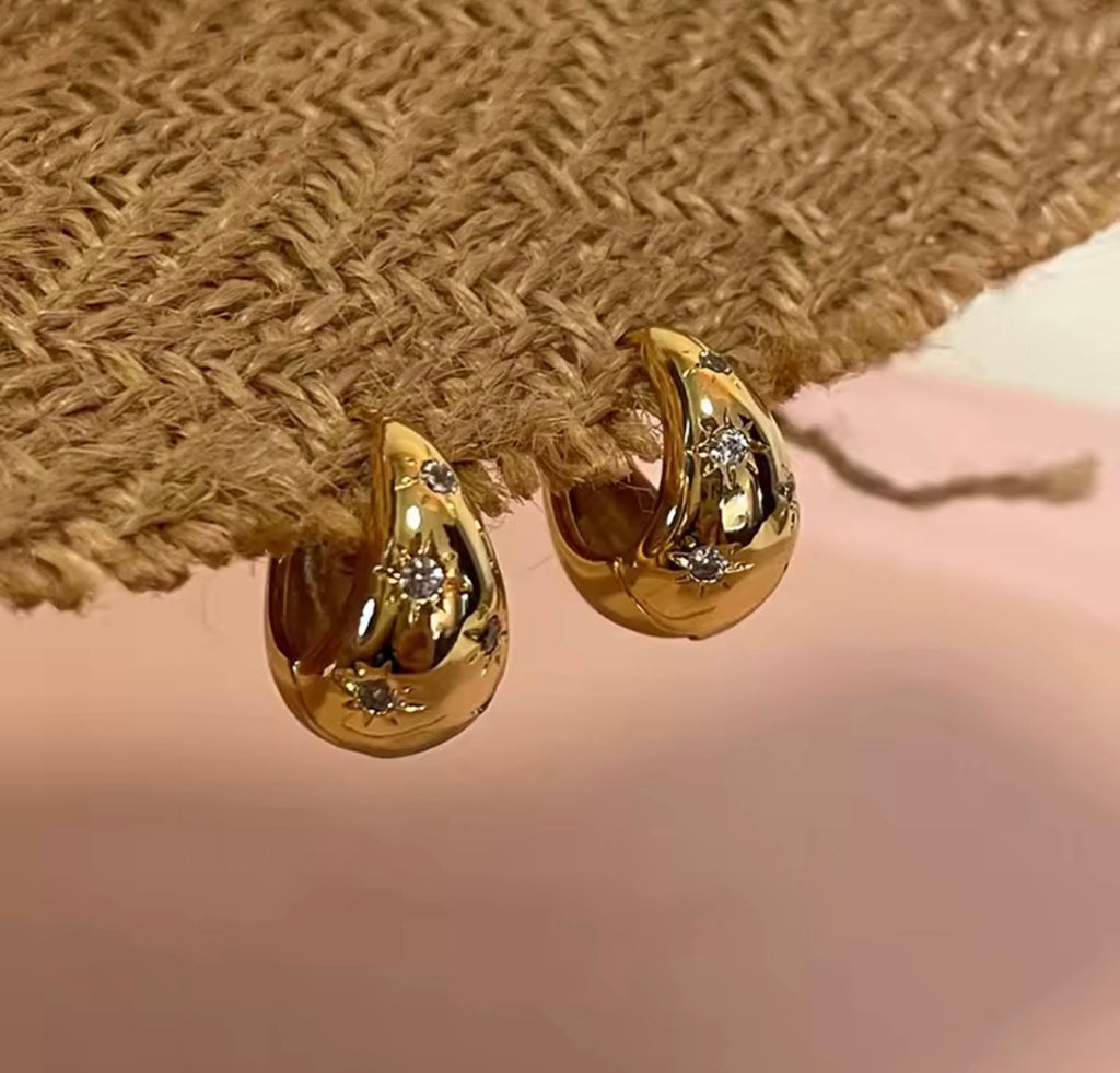  The Astra Chunky Gold Star Hoop Earrings on  beige background