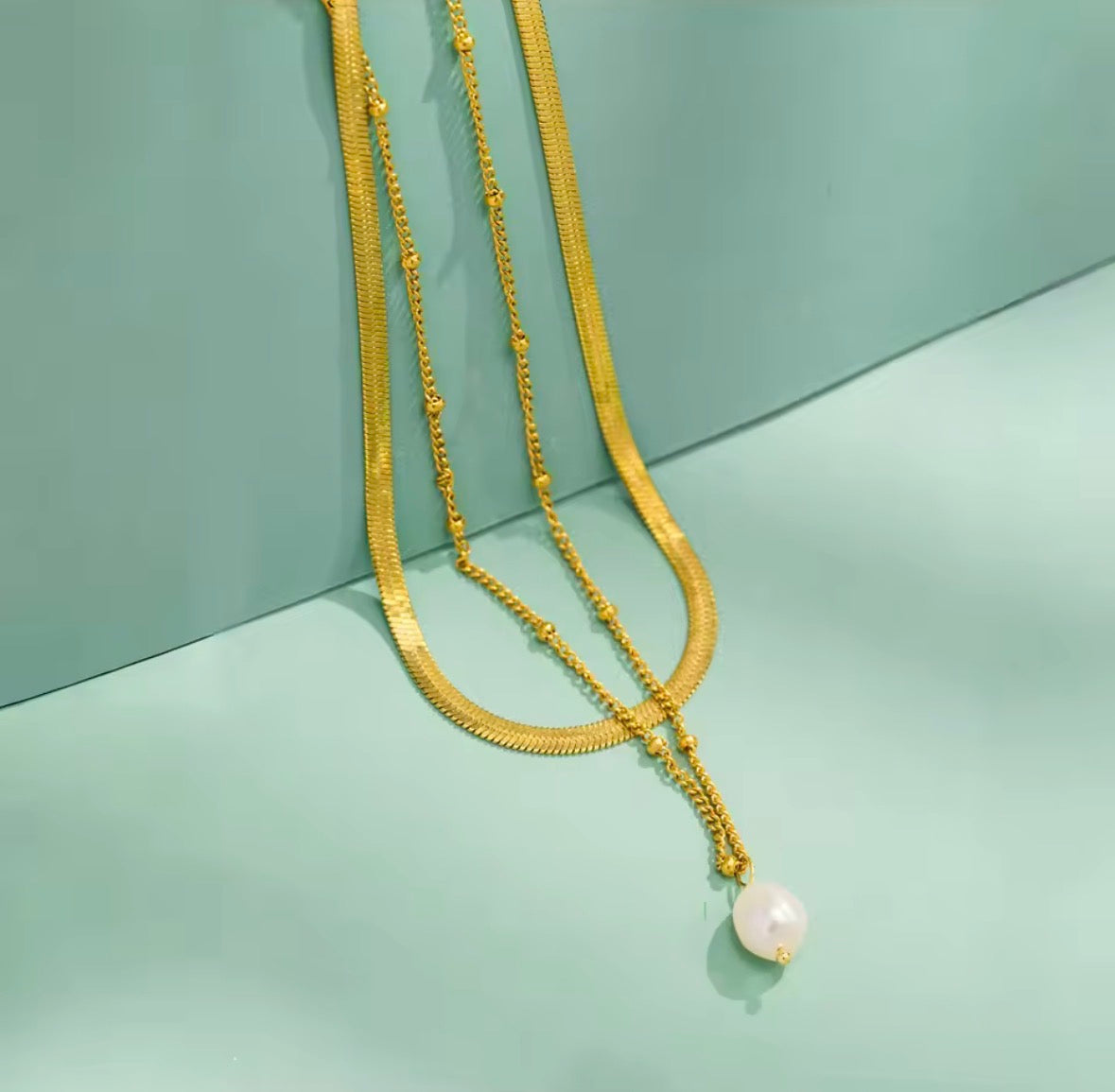 Gold necklace with a pearl pendant on a light green background