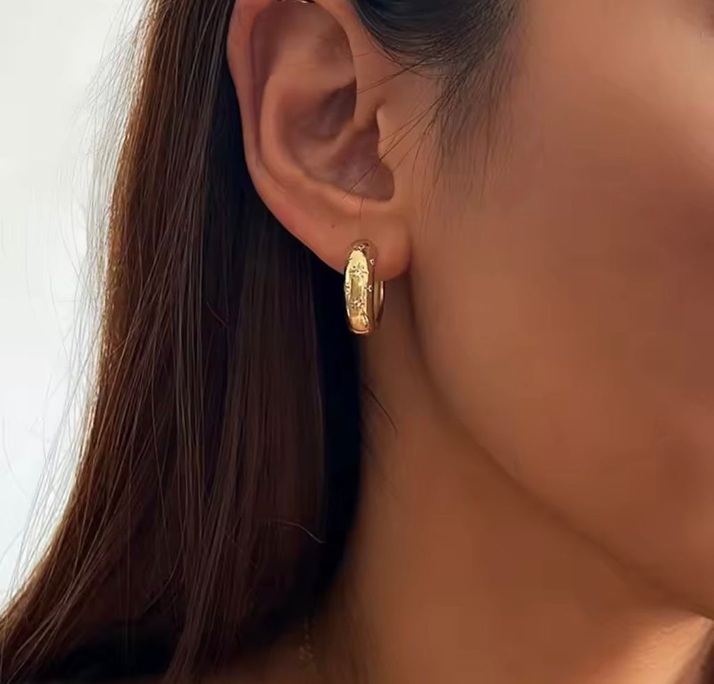 The Aurora Hoops Close-up of a person wearing a gold hoop earring with a blurred background