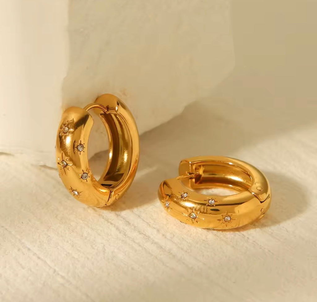 The Aurora Hoops Gold hoop earrings with embedded stones on a beige fabric background