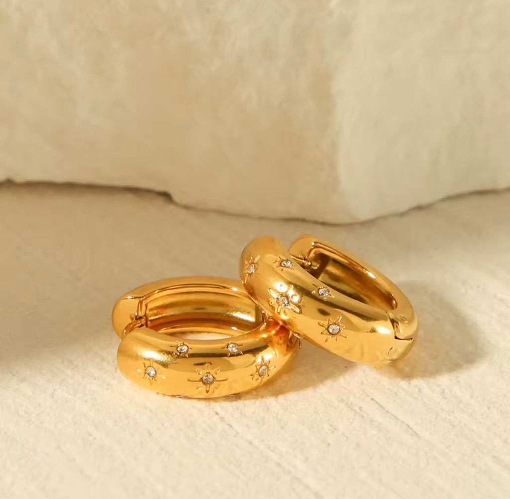The Aurora Hoops Gold hoop earrings with embedded stones on a beige surface