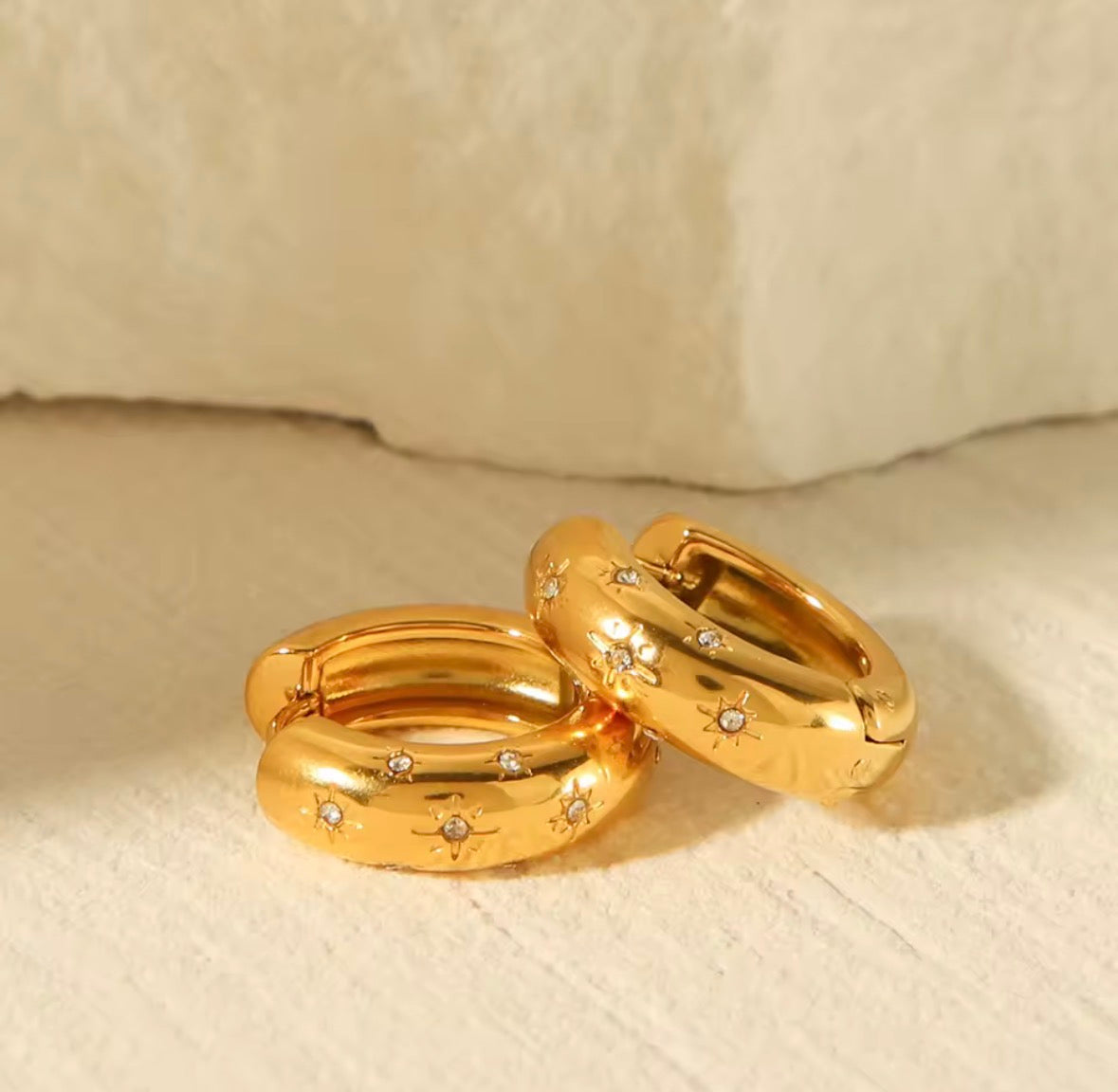 The Aurora Hoops Gold hoop earrings with embedded stones on a beige surface