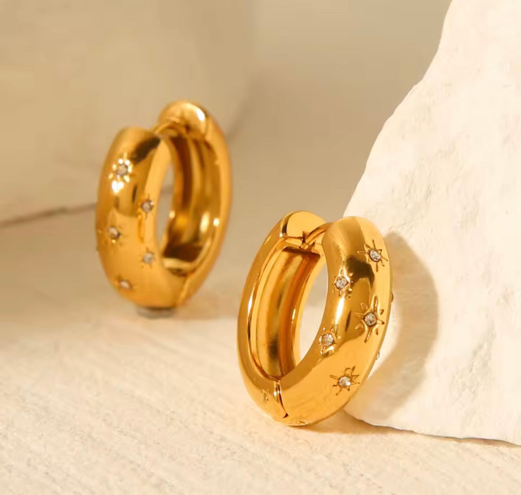 The Aurora Hoops Gold hoop earrings with embedded stones on a textured beige surface