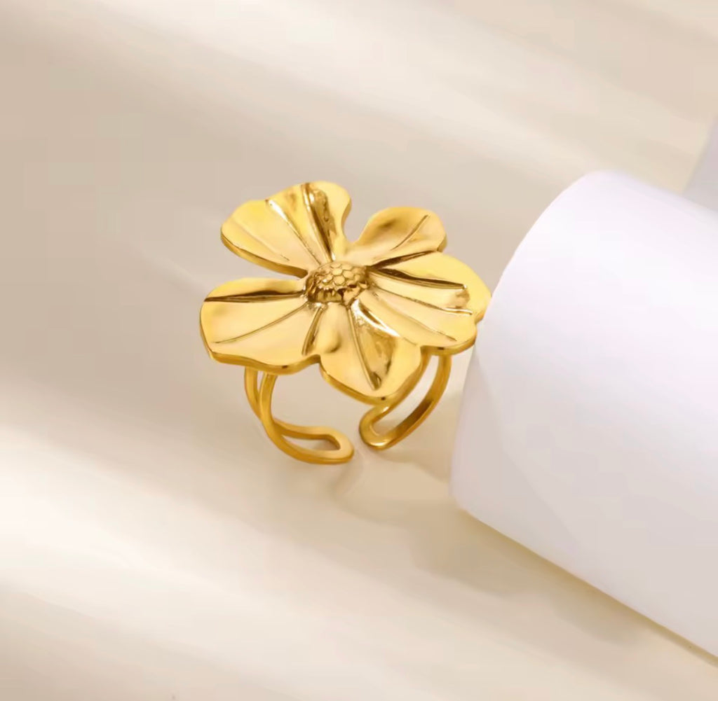 The Camellia Ring Gold flower-shaped ring on a beige background