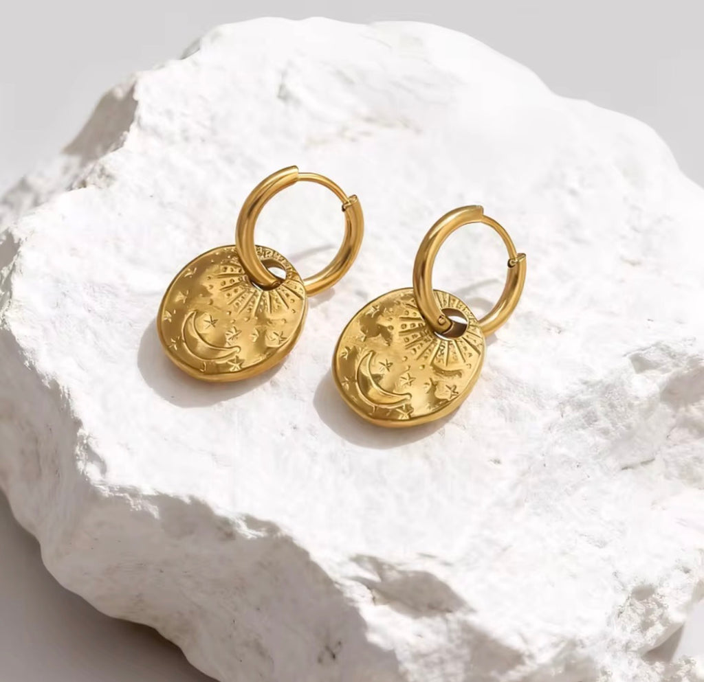 The Celeste Hoops  Gold hoop earrings with circular designs on a textured white surface