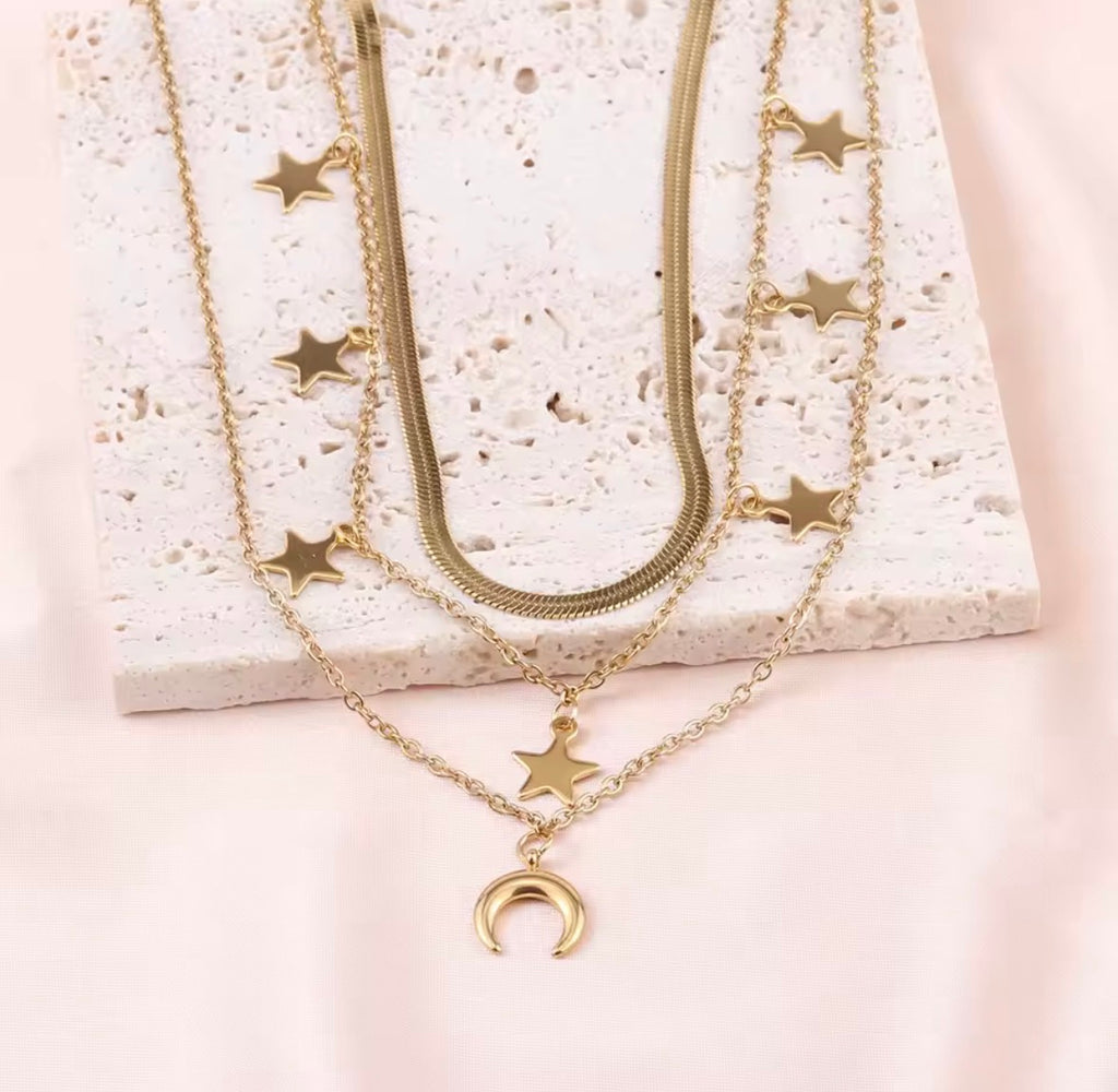 The Celestia Necklace  Gold necklaces with star and moon pendants on a textured white surface