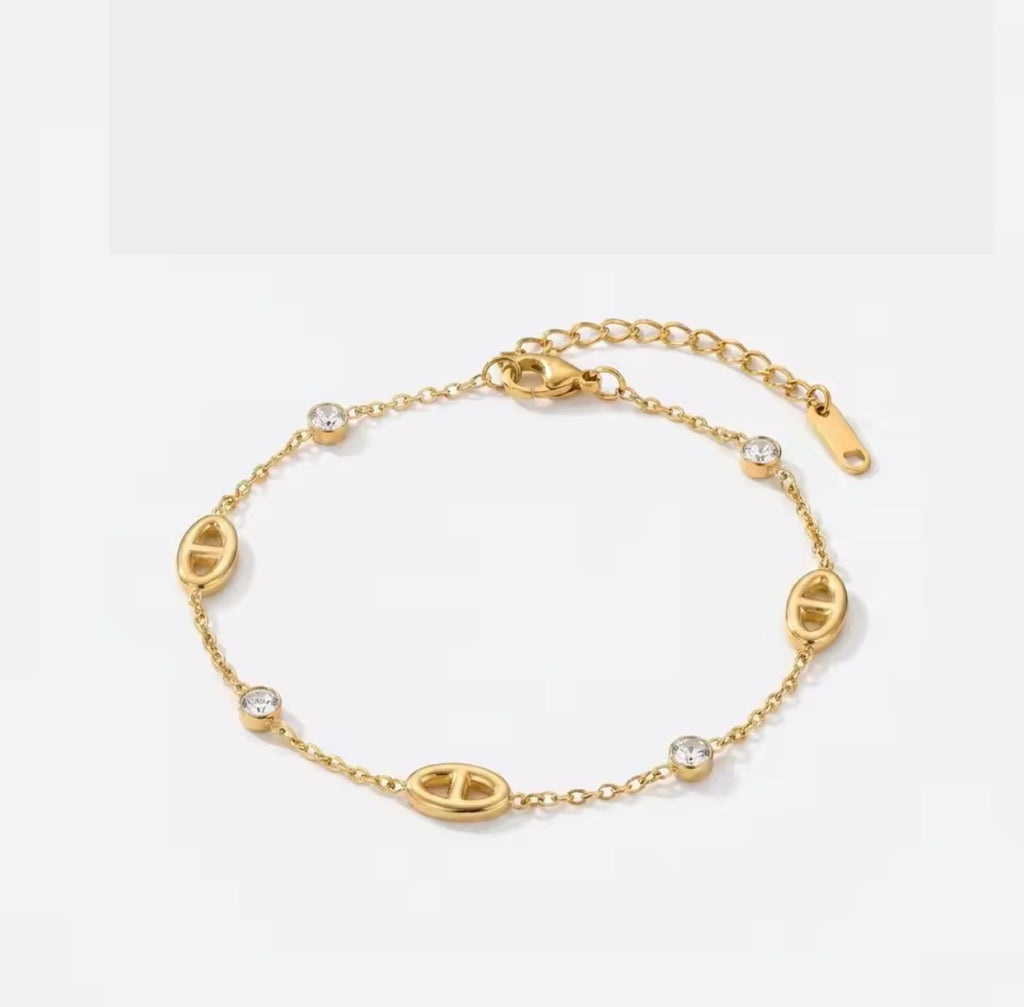 Shop The Celestine Bracelet – an elegant gold-tone stainless steel bracelet with geometric oval motifs and sparkling white zircon accents. Adjustable and hypoallergenic.