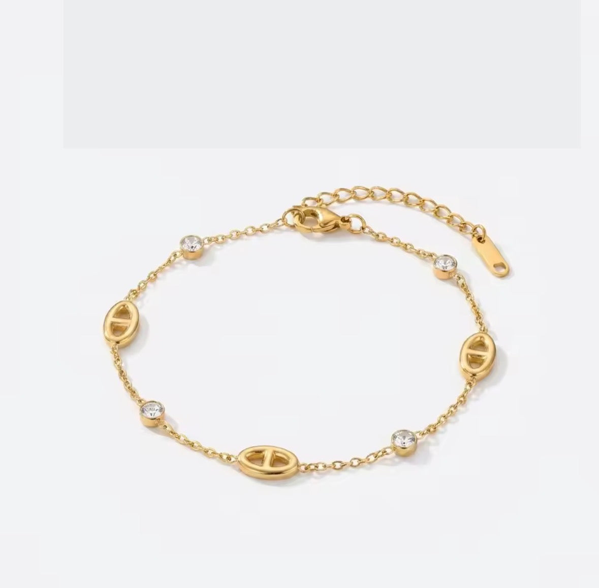 Shop The Celestine Bracelet – an elegant gold-tone stainless steel bracelet with geometric oval motifs and sparkling white zircon accents. Adjustable and hypoallergenic.