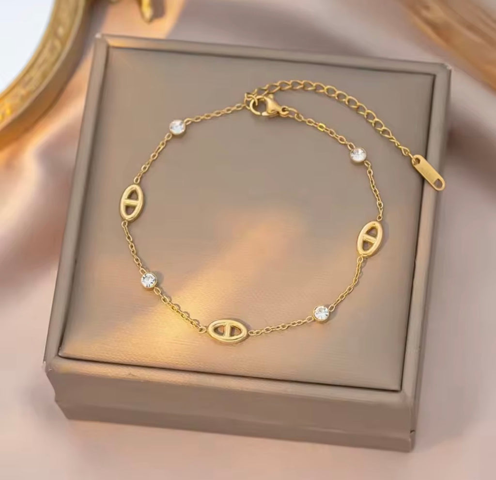 Shop The Celestine Bracelet – an elegant gold-tone stainless steel bracelet with geometric oval motifs and sparkling white zircon accents. Adjustable and hypoallergenic.