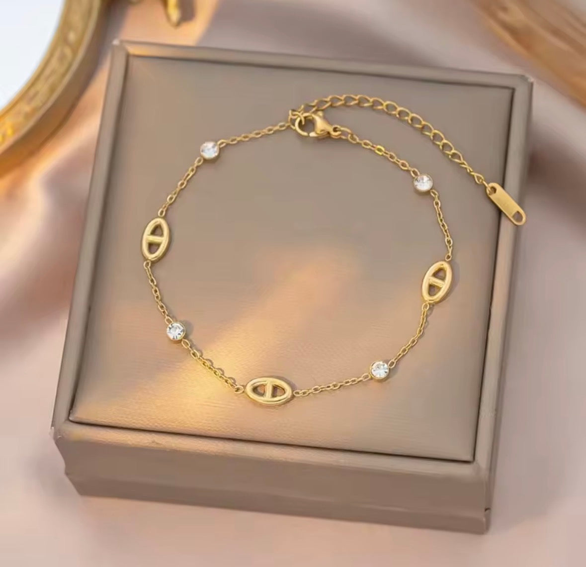 Shop The Celestine Bracelet – an elegant gold-tone stainless steel bracelet with geometric oval motifs and sparkling white zircon accents. Adjustable and hypoallergenic.