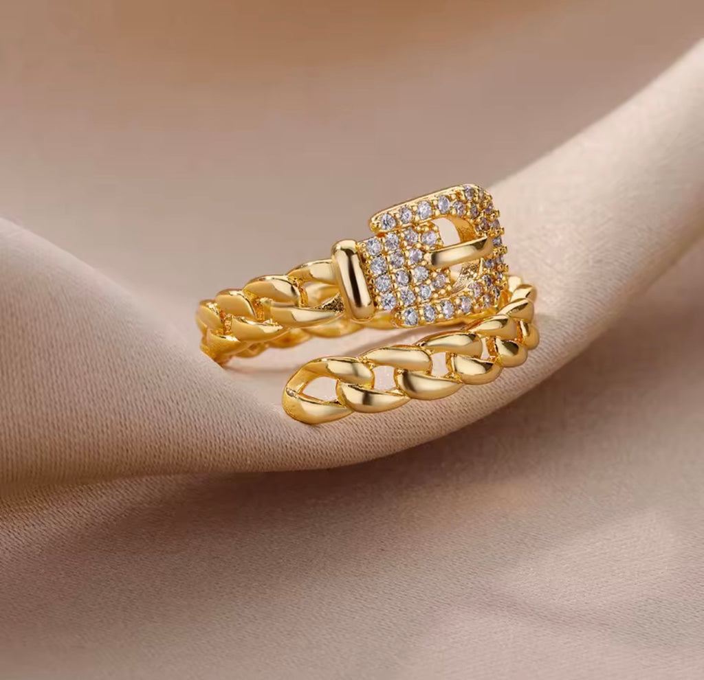 The Cintra Ring with chain design and diamond accents on a beige fabric background