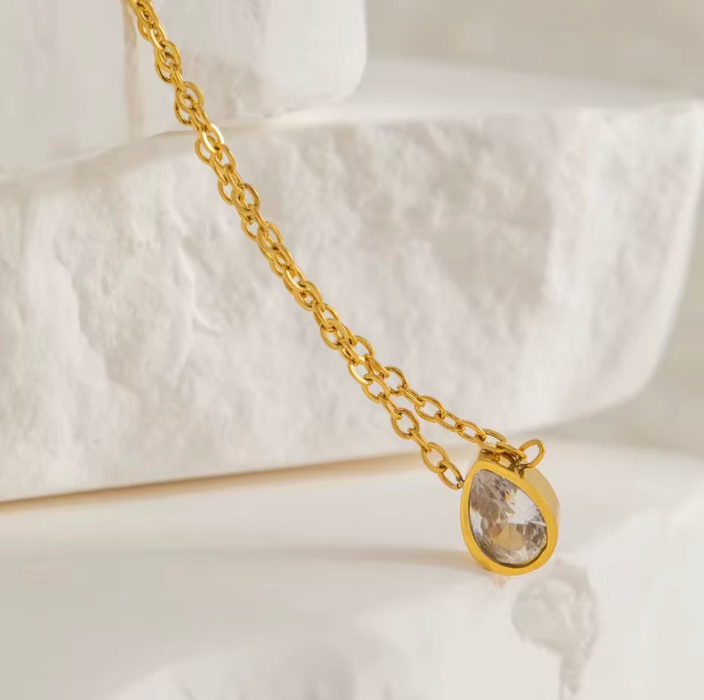 Gold necklace with a teardrop-shaped pendant on a white background