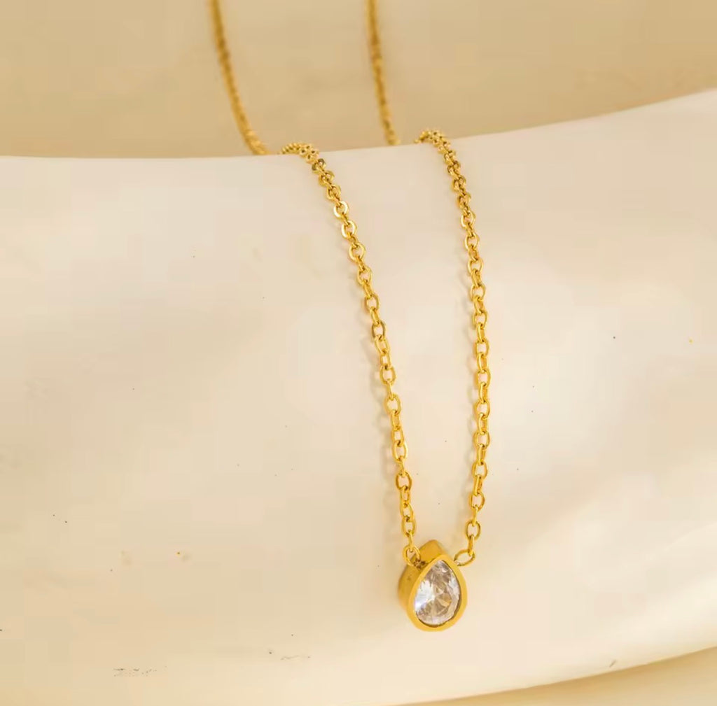 Gold necklace with a teardrop-shaped pendant on a beige background
