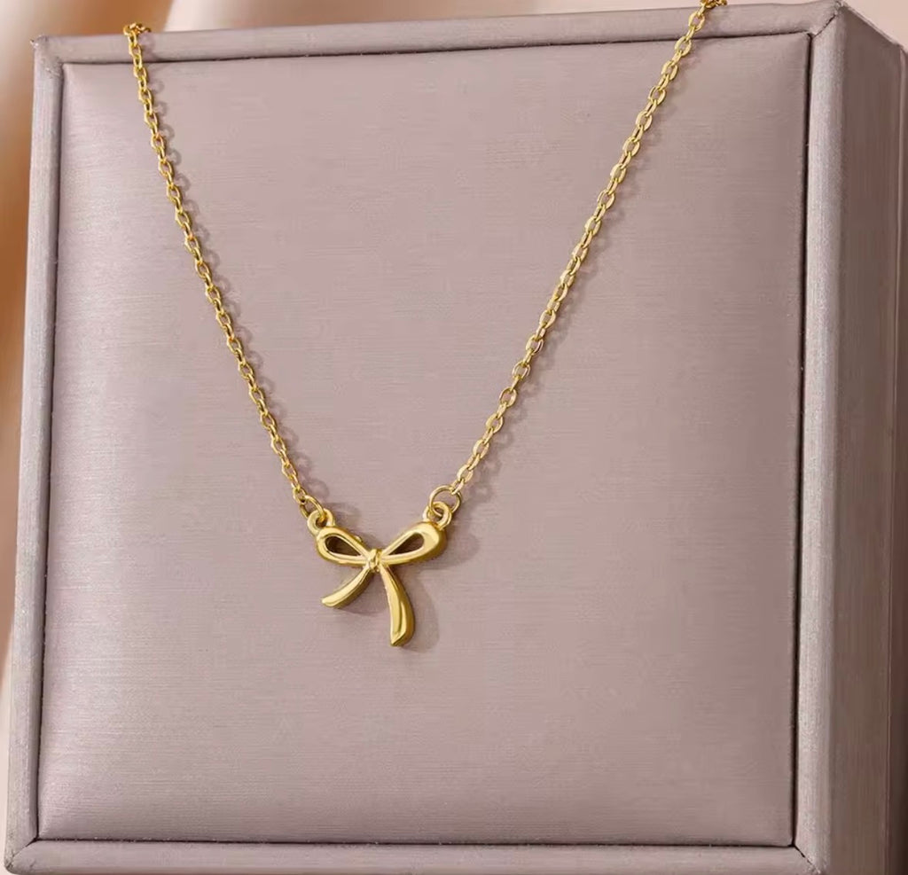 The Eloise Necklace: Gold bow-shaped necklace on a gray box