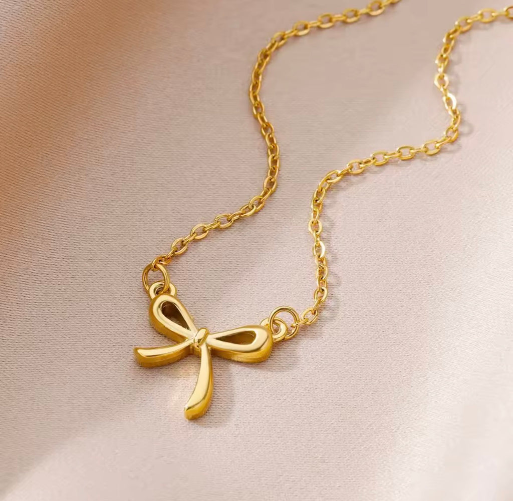 The Eloise Necklace Gold bow-shaped necklace on a soft beige background