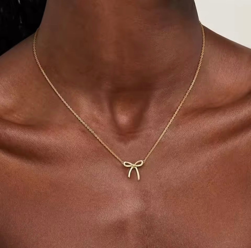 The Eloise Necklace Gold necklace with a bow pendant on a person's neck
