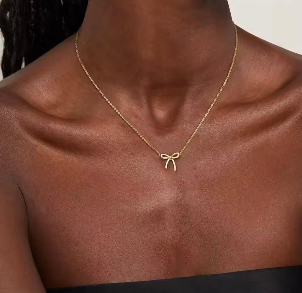 The Eloise Necklace Gold necklace with a bow pendant on a person's neck against a neutral background