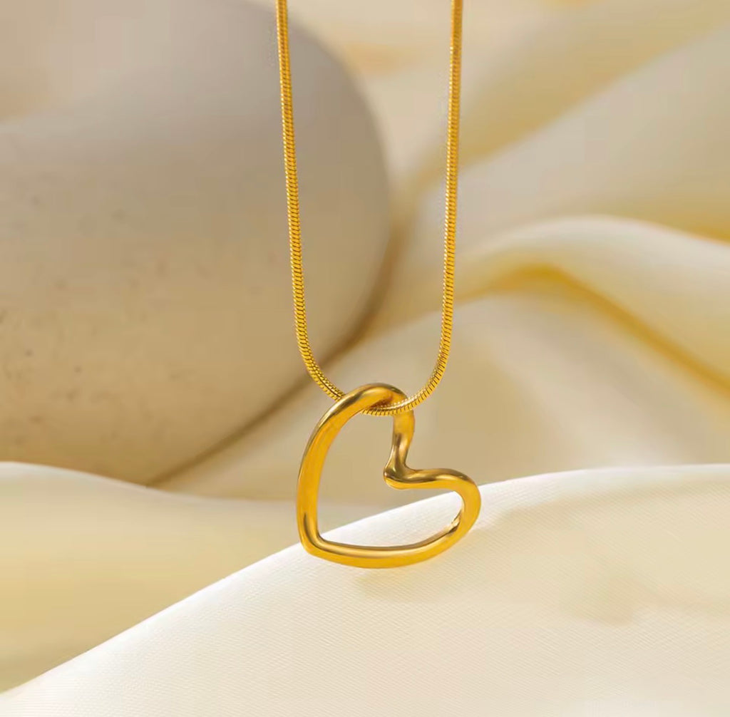 The Esmé Necklace Gold heart-shaped necklace on a beige fabric background