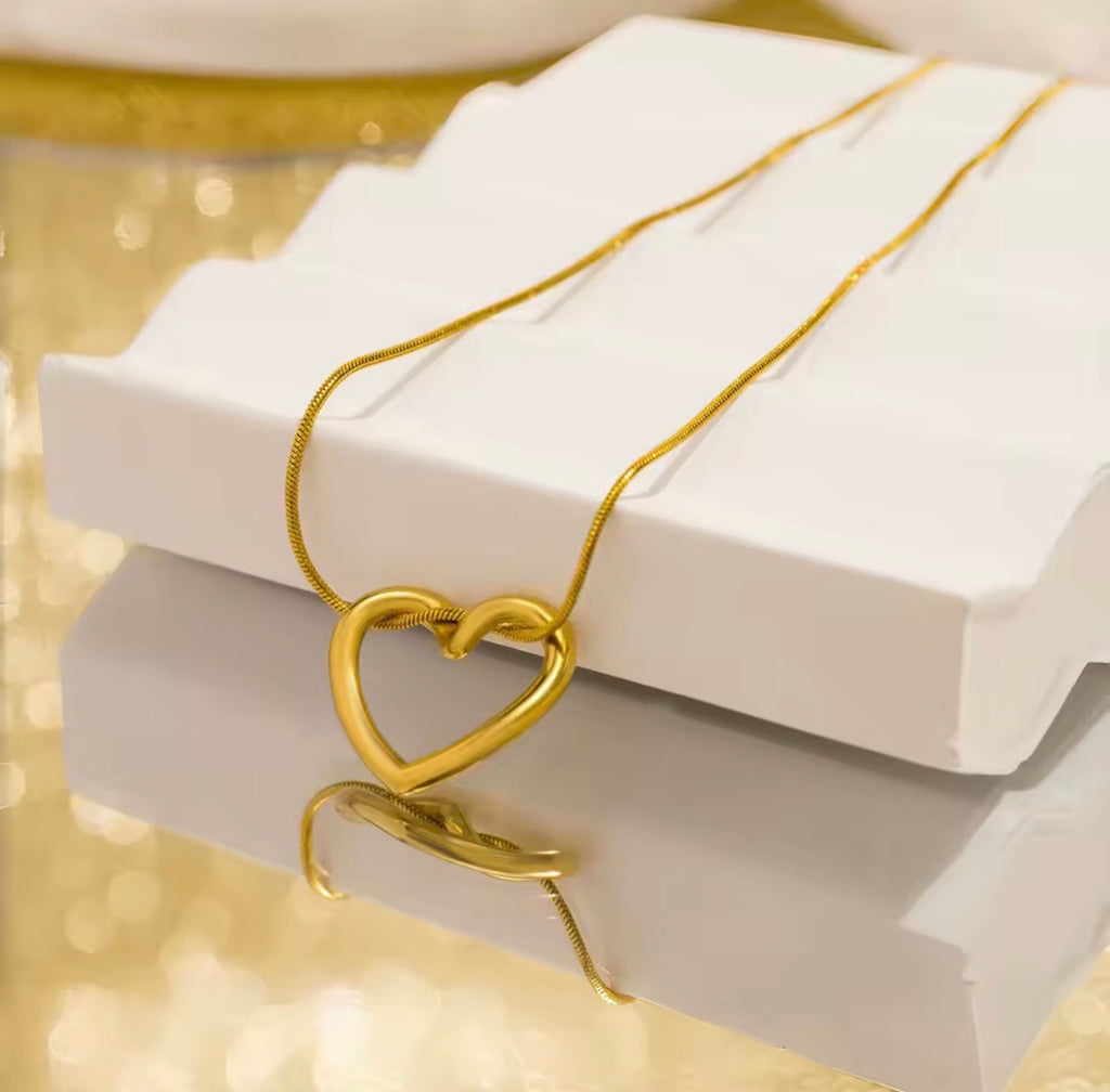The Esmé Necklace Gold heart-shaped necklace on a white box with a gold background
