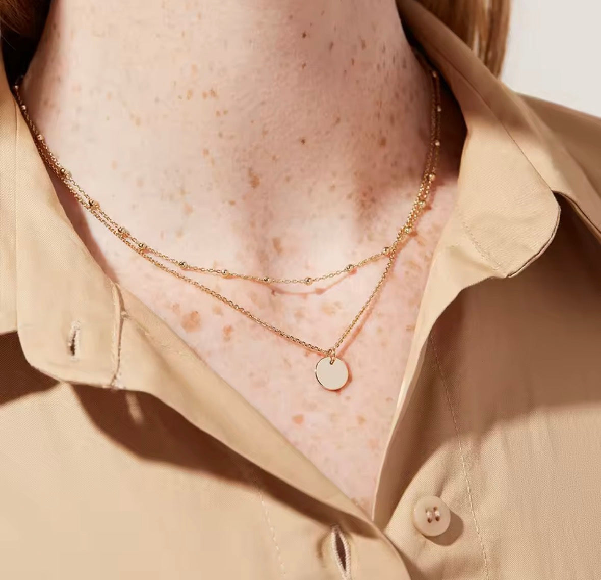 The Evienne Necklace Close-up of a person wearing a gold necklace with a beige shirt.