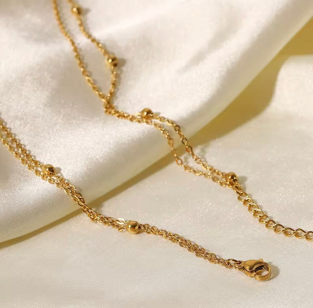 The Evienne Necklace  Gold chain necklace on a white fabric background