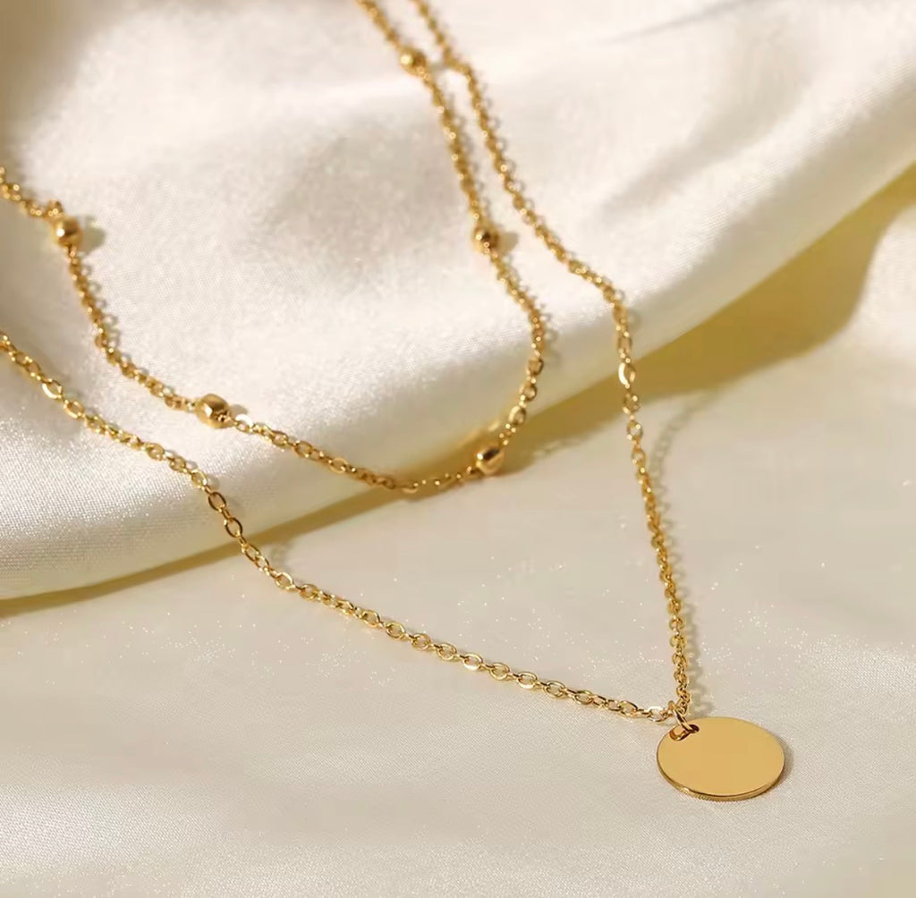 The Evienne Necklace Gold necklace with a round pendant on a white fabric background