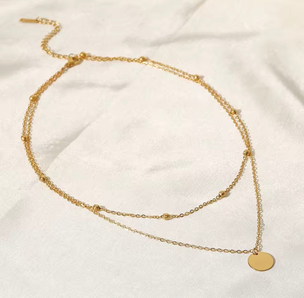 The Evienne Necklace Gold necklace with round pendants on a white fabric background