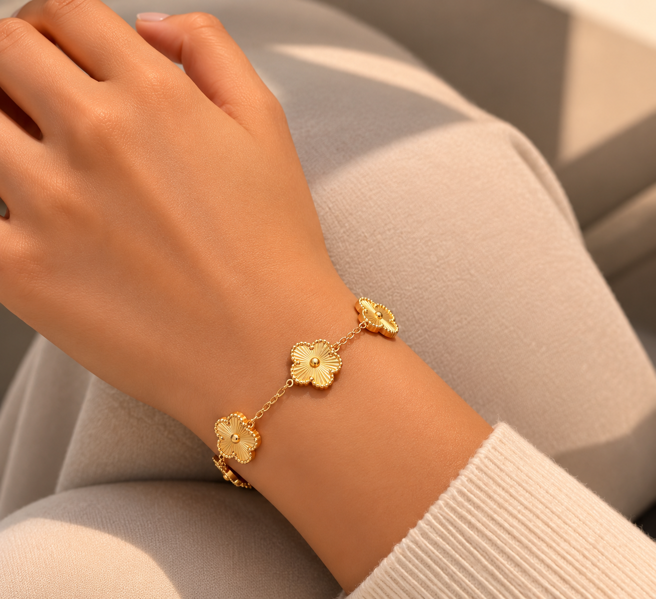 The Fiore Bracelet   A delicate gold chain bracelet with three textured flower charms worn on a person's wrist, shown against a soft beige background.
