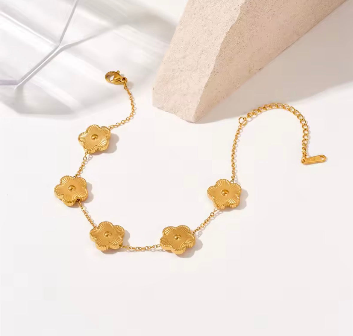 The Fiore Bracelet  A gold chain bracelet featuring five textured flower-shaped charms, displayed on a clean white surface with a light beige stone prop.