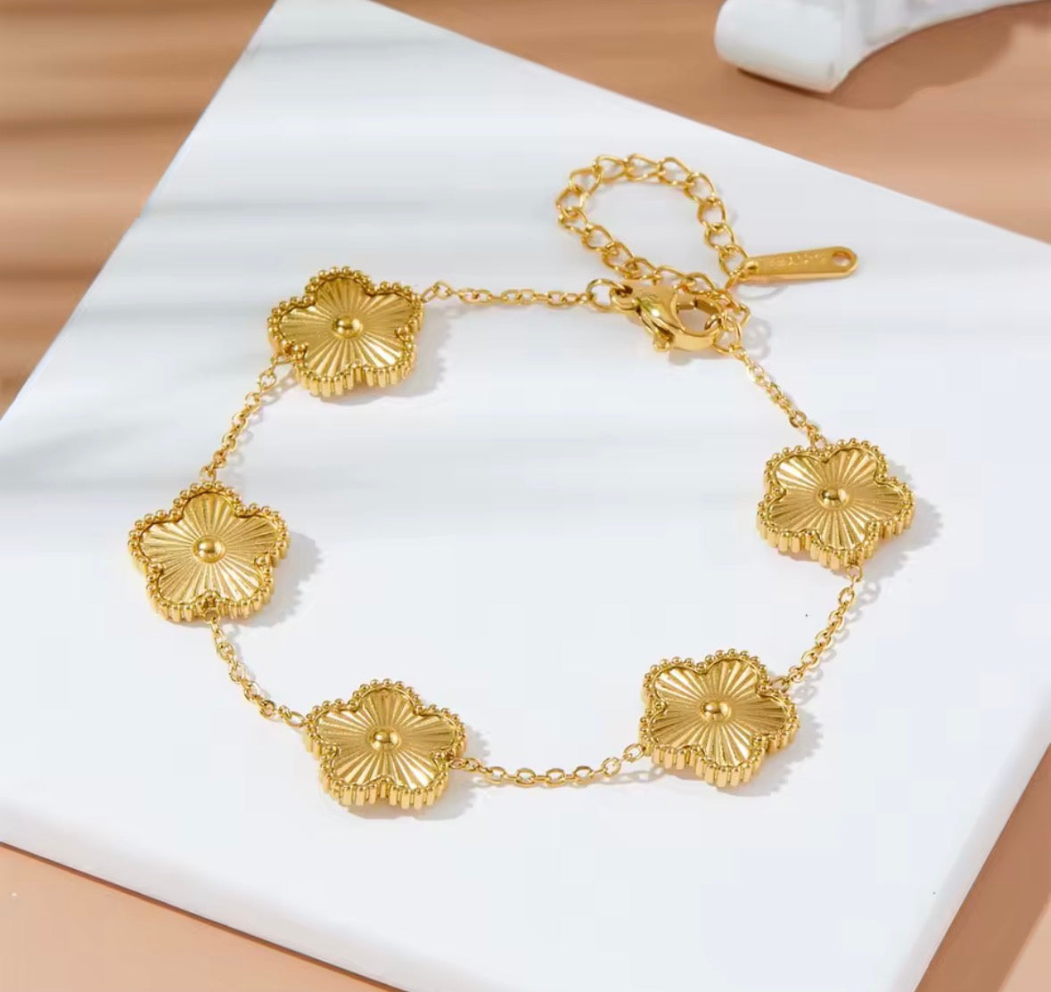 The Fiore Bracelet A gold chain bracelet with five textured, flower-like oval links, displayed on a white square card with soft shadows.