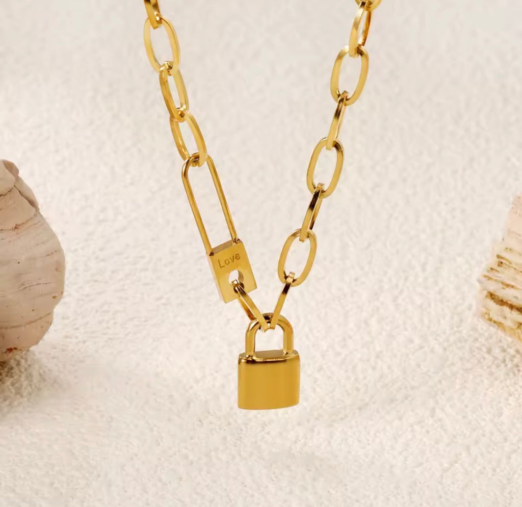 The Heartlock Necklace Gold chain necklace with padlock charm on a textured beige background