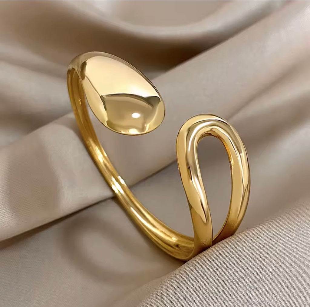 The Imperia Bangle Gold bracelet on a beige fabric background