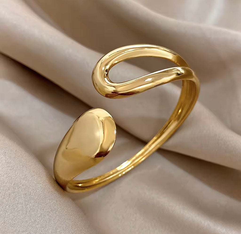 The Imperia Bangle Gold bracelet on a beige fabric background