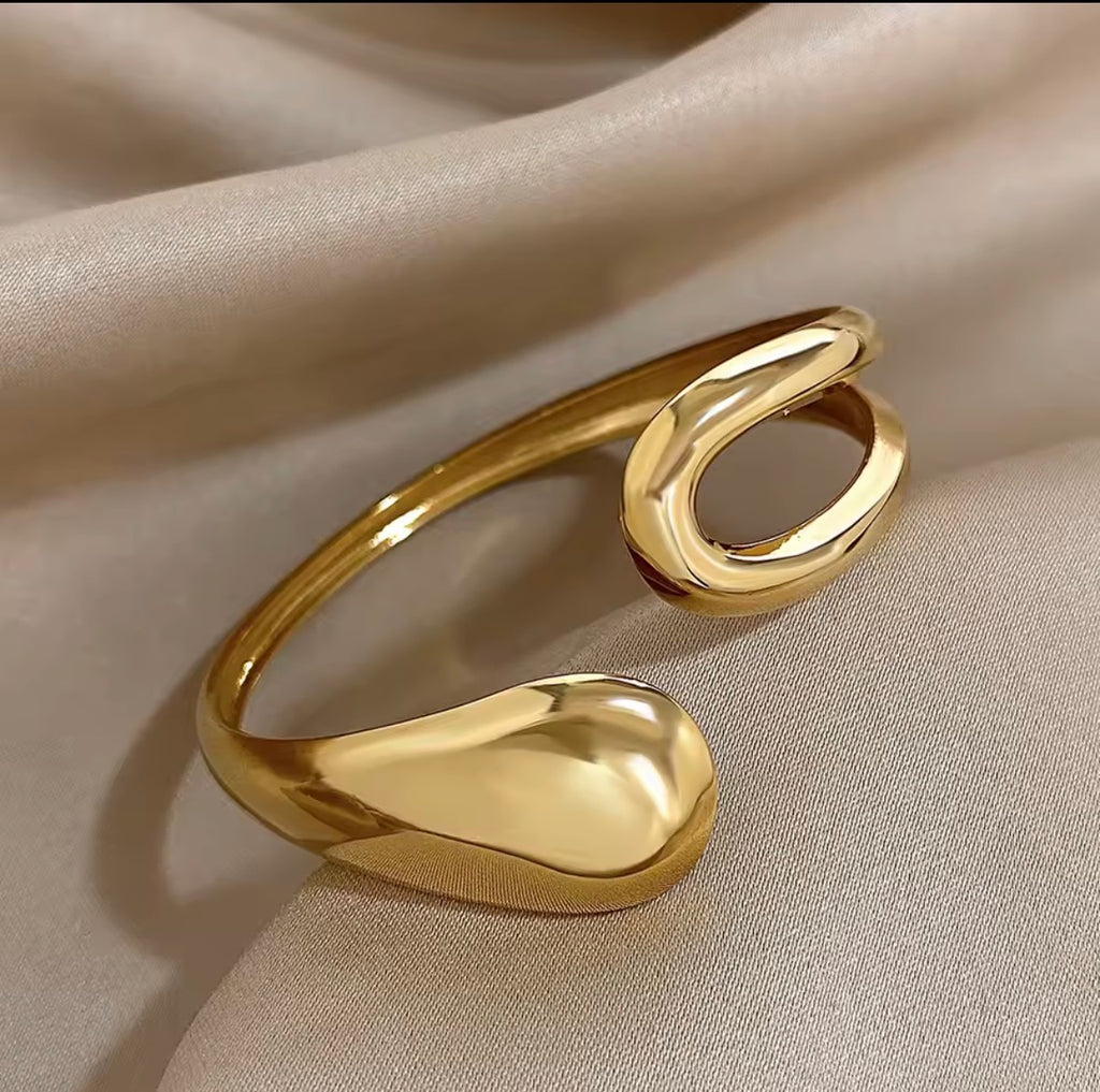 The Imperia Bangle Gold bracelet on a beige fabric background