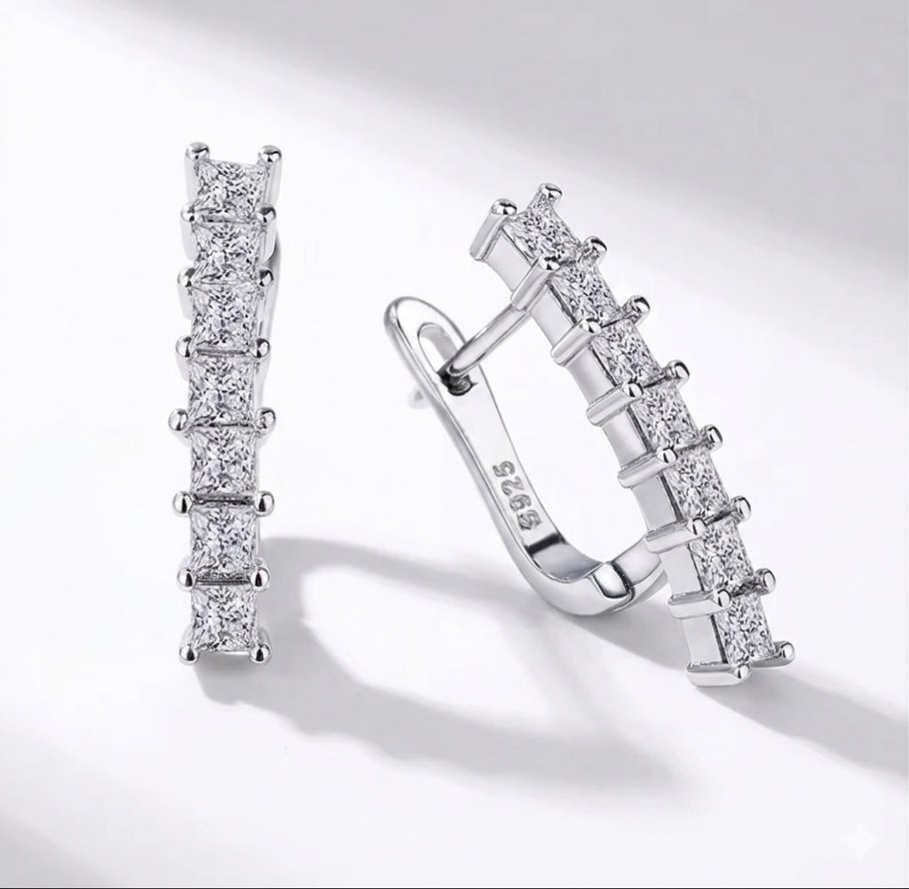 The Isabella Studs Pair of silver hoop earrings with clear gemstones on a light gray background