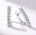 The Isabella Studs Pair of silver hoop earrings with clear gemstones on a light gray background