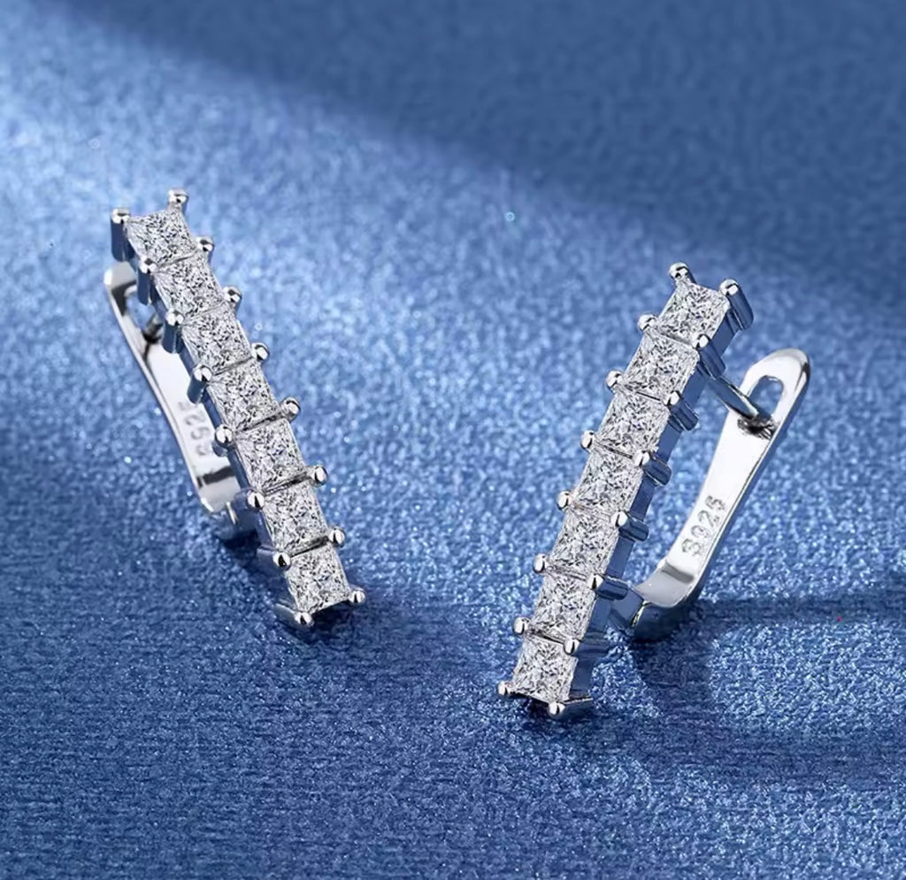 The Isabella Studs Silver earrings with clear stones on a blue textured background