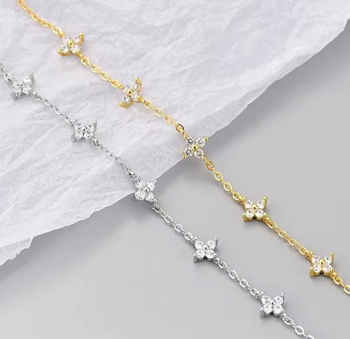 The Linnea bracelet: Gold & Silver Two delicate chain bracelets with small butterfly motifs, one in yellow gold and one in silver, displayed on a textured white paper background.