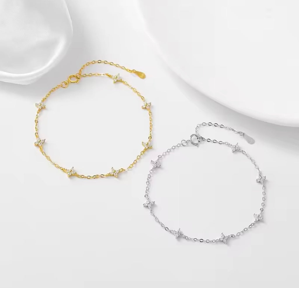 The Linnea bracelet Two delicate chain anklets with small star charms, one in gold and one in silver, displayed on a clean white surface with soft shadows.