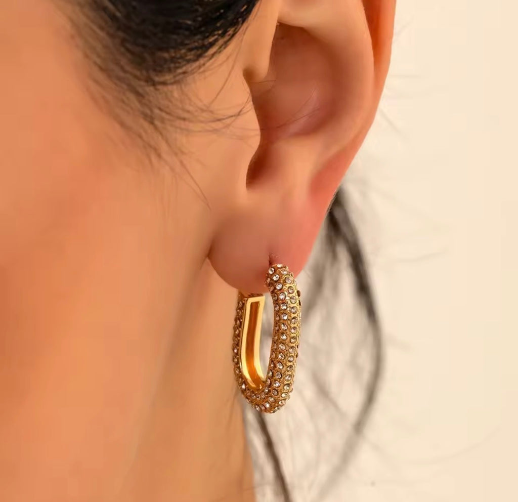 The Lyra Huggies Close-up of an ear wearing a gold hoop earring with small stones.