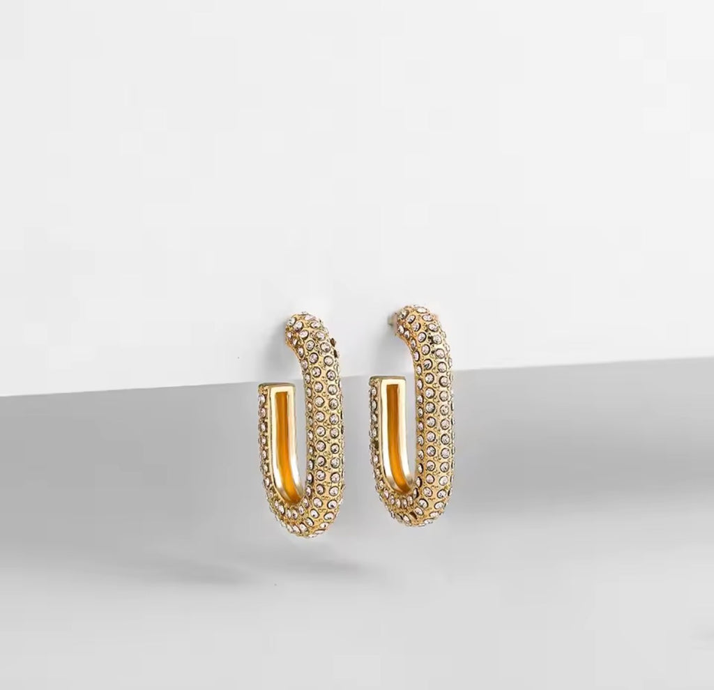 The Lyra Huggies Gold hoop earrings on a light gray surface with a white background