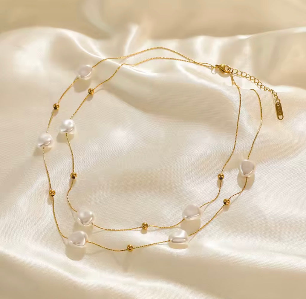 The Mirabelle Necklace Gold necklace with pearls on a beige fabric background