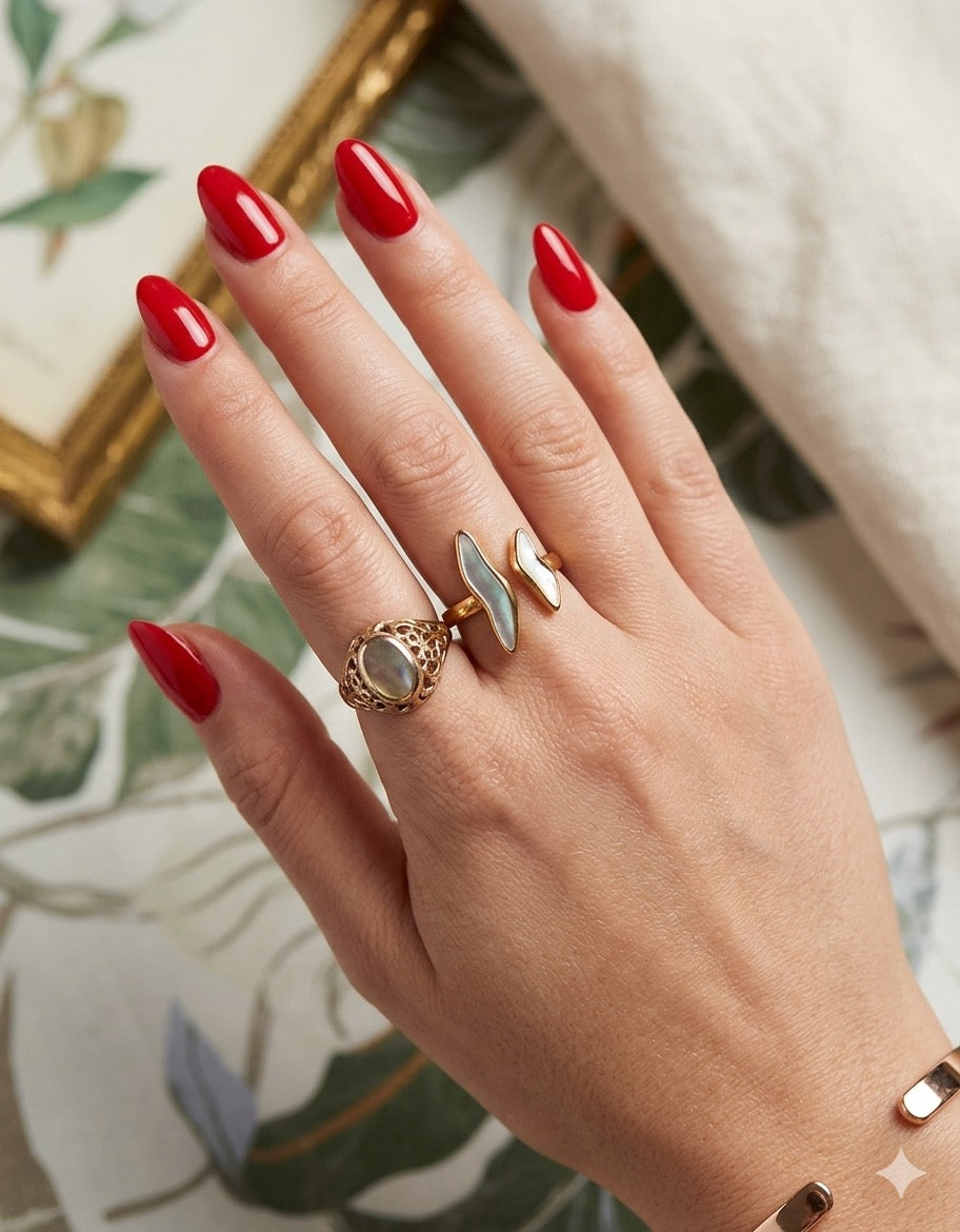 The Ondine Ring Hand with red nail polish wearing two rings against a decorative background